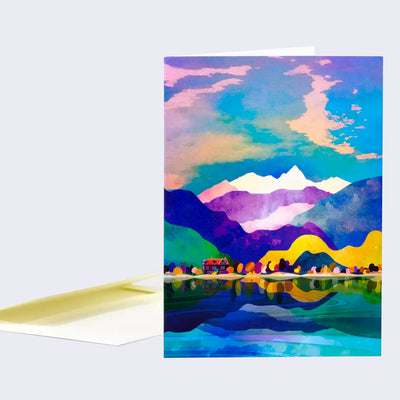 Greeting card with a colorful full bleed illustration of a cloudy sky over a scene of many mountain ranges and a small forest house on a lake.