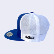 Side view of royal blue baseball cap. The entire back side of cap is white mesh. Cursive text embroidered on left side of cap says giant robot.