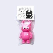 Hot pink vinyl figure character, standing with arms at its side. It has a round head with curved horns and simple angry eyes with no other facial features. It has a white sparkle on its upper right chest. Character is inside of a plastic bag with a white hang tag that says "Big Boss Uamou" with an illustration of the figure.
