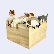 5 different plastic cat figures, all strewn over a ledge in a variety of poses. Designs include, Siamese laying on its back, white cat sleeping on its belly with back leg hanging off, Calico cat sitting upright, white and orange cat crawling onto and finally gray and white cat clinging to edge.
