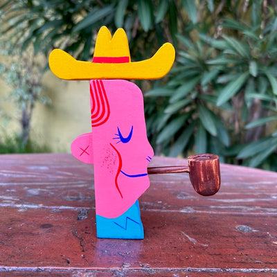Die cut wooden sculpture of a mid western looking man, with a cowboy hat and smoking a pipe. It has its eyes closed and a slight smile.