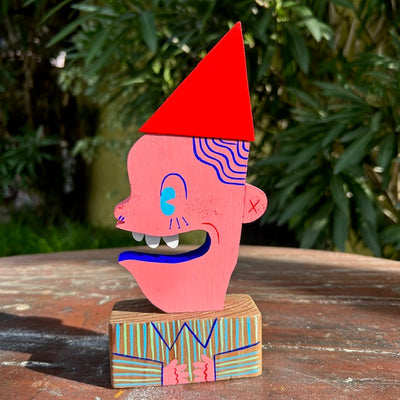 Die cut painted wooden sculpture of a pink person, looking off to the side with a wide open mouth smile. Its head is on a wooden block designed line a striped button up.