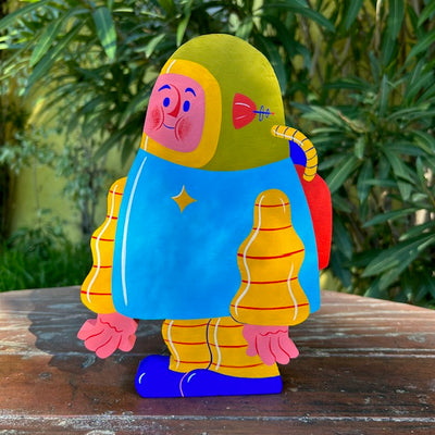 Die cut painted wooden sculpture of a chubby person in a blue space suit, with a green helmet, yellow arms and legs and a red air tank.
