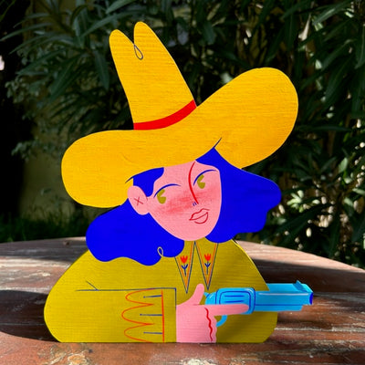 Die cut painted wooden sculpture of a blue haired girl in a tall cowboy hat, wearing a olive green shirt and holding a pistol, faced to the right.