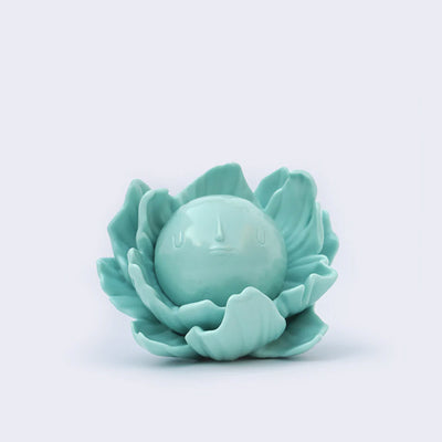 Turquoise vinyl figure of a round full moon with a small minimalistic face. It sits within a series of flower petals, as if it is the pistil of the flower.