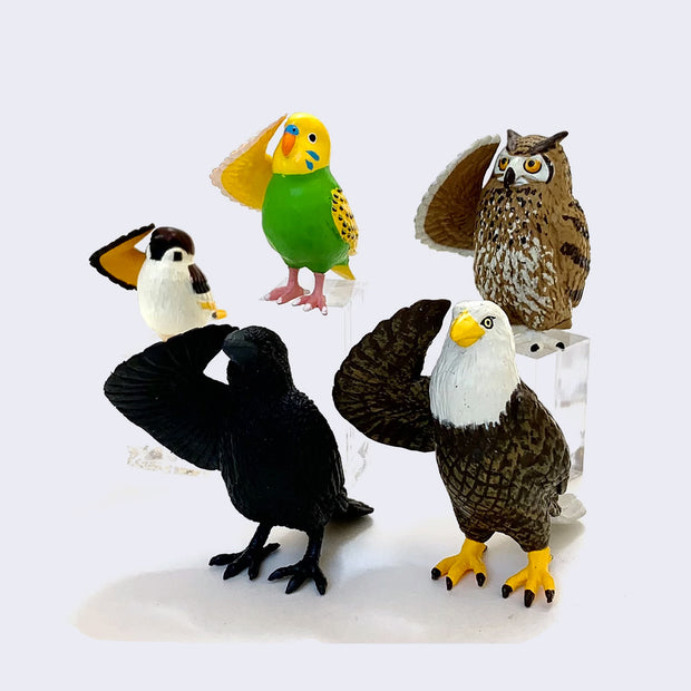 5 small plastic figures of birds, all standing and saluting with one wing. Bird types are: sparrow, parakeet, owl, crow and eagle.