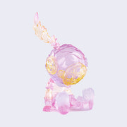 Semi transparent sculpted figure of a small person sitting with their hands at their side, legs out in front of them and wearing a scuba diving helmet with a feather coming out of the top. Figure is primarily light purple with yellow ombre elements.