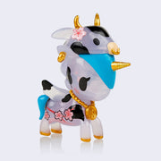 Vinyl semi transparent unicorn figure with subtle glitter injection. It has black blotches on its body, like a cow pattern, a blue mane and tail and a gold hoop earring and medallion chain around its neck. Atop its head is an ox head with gold horns and gold septum ring.