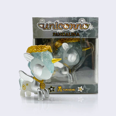 Vinyl unicorn figure next to its display box which is partially clear to be able to see the figure while boxed. Figure is a unicorn, half silver and half semi translucent with gold necklace, horn and leaf crown on its head.