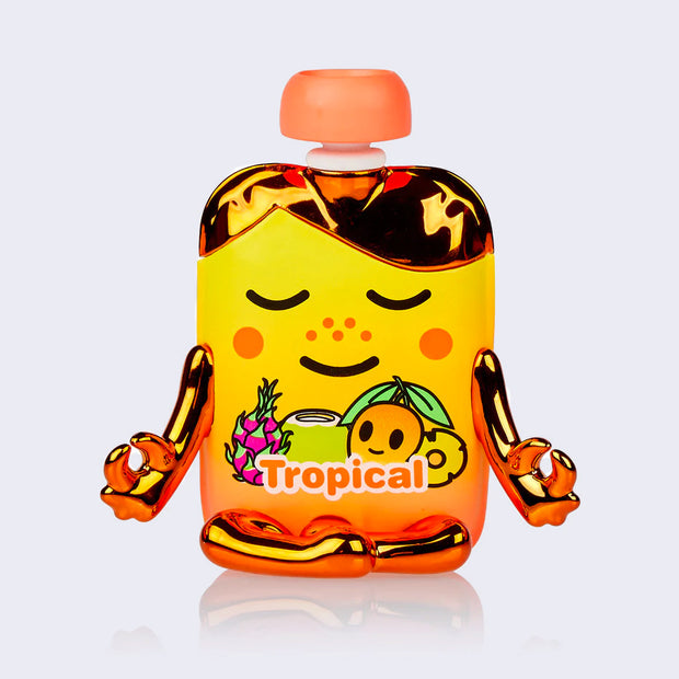 Vinyl figure of a cartoon style apple sauce pack, tropical flavored. It is sunset yellow and orange with gold metallic elements and is in a meditation pose, with a smile on its face.