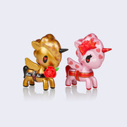 2 vinyl unicorn figures, one hold with a rose in its mouth and a rose in their mouth and "love you" written across its side. Other is pink with red hearts and bow on its ear and wrapping its body, with "love" written on its face.