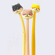 3 rubber coated pens with cartoon shiba inu heads with pink cheeks as pen toppers. Shiba colors include black, brown and yellow.