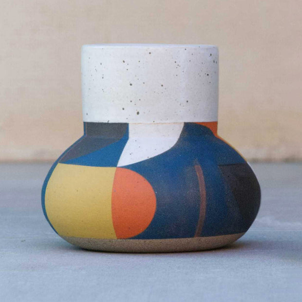Ceramic pot with a wide top opening, white and speckled. The bottom is painted in large geometric shapes of blue, orange, yellow and brown.