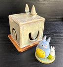 Set of ceramic sculptures, one cube shaped and modeled to look like Totoro. Nearby are a small blue and white chibi Totoro, standing on a small circle platform with a grass tuft.