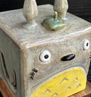 Close up of a ceramic cube shaped and modeled to look like Totoro. 