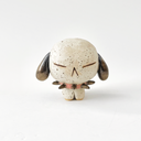A small speckled ceramic figurine of a dog-like character with closed eyes, brown floppy ears, and a pink spiked collar, centered on a plain white background.