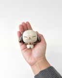A small speckled ceramic figurine of a dog-like character with closed eyes, brown floppy ears, and a pink spiked collar, centered on a plain white background.