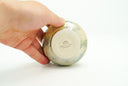 Small ceramic pot with a cream colored and light green glossy exterior with many small divets like the surface of a moon.