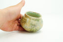 Small ceramic pot with a cream colored and light green glossy exterior with many small divets like the surface of a moon.