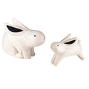 Two white wood figurines of rabbits, one is slightly larger than the other.