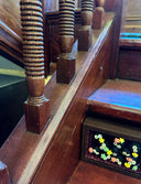 Diorama style sculptural work of many black soot sprites holding colorful stars. They're within a wooden box with red fabric lining it. Piece is under the stairs.