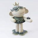 A handmade ceramic figurine of a stylized girl with a crown, short hair like ocean waves, and her hand extended out, with a tiny sailboat on her arm. Her dress has a fish pattern.