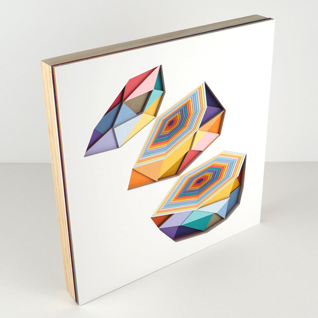 Geometric designed layered cut paper sculpture, creating a three dimensionality. A multi sided shape is cut into 3 layers, with each layer showing the cross section of several layers of cut paper. Colors are earthy toned blues, oranges, yellows, purples and reds.