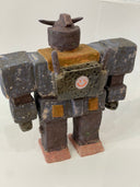 Ceramic sculpture of a Gundam with a wide, blocky body and several buttons and suit detailing with a pointed helmet.