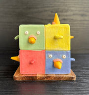 Ceramic cube made up of 8 different colored cubes: green, yellow, red and blue. Bird beaks come out of one side and little wings come out of other sides.