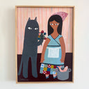 A framed folk art painting on canvas featuring a black cat holding a bouquet of flowers next to a woman in a blue dress and patterned apron, with a pink fish in a pot at her feet. The painting is housed in a light wood frame and hangs on a white wall.