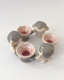 A circle of 6 ceramic figures, linked by their hands. 3 are small cartoon characters, the other 3 are flowers with arms.