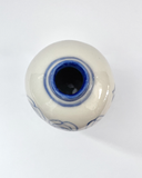 A small round ceramic vase viewed from above, featuring a glossy off-white glaze with blue painted floral details and a dark blue interior opening, set against a plain white background.