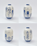 Four views of a small ceramic vase with a glossy white body and blue hand-drawn cartoon characters, shown on a light gray studio background.