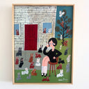 A framed folk art painting on canvas depicting a woman sitting on a stool, smoking a cigarette, surrounded by numerous rabbits in front of a house, enclosed in a light wood frame and hung on a white wall.