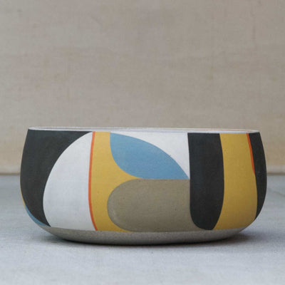 Short ceramic bowl. The natural light tan clay color shows through with large painted geometric shapes over it in yellow, white, blue and black.