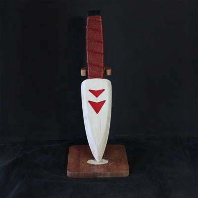 Whittled wooden sculpture of a knife, turned down and onto a stand. The blade of the knife is white with red arrow patterning and the handle is leather bound.
