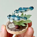 Two small blue fish figurines on a circular wooden base with leaves and a stone.