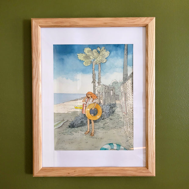 Ink and watercolor illustration of a orange haired girl standing on the entrance to a beach, holding a yellow inflatable tube. Some palm trees line the background and the sky is clear. Piece is matted into a thin wooden frame.