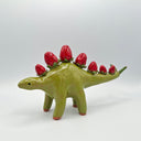 Green ceramic stegosaurus with red strawberries for spikes on a white background