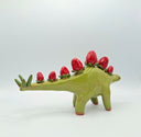 Green ceramic stegosaurus with red strawberries for spikes on a white background