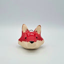 Small ceramic sculpture of a red fox's head with white ears and chin fur. It has a small curved wire atop its head, for hanging.