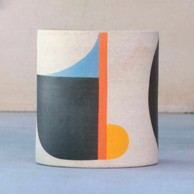 Ceramic cup, without any curvature. The natural light tan clay color shows through with large painted geometric shapes over it in orange, blue and black.