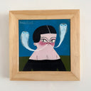 A framed painting featuring a stylized illustration of a woman with black hair, a pink face, and two blue ghostly figures coming out of her mouth, shaped like snakes on a blue background, housed in a light wood frame.