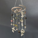 A hanging decorative mobile made from ceramic mini sculpts, small natural stones and bead charms on silver chains, photographed against a plain gray background.