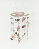 A hanging decorative mobile made from ceramic mini sculpts, small natural stones and bead charms on silver chains, photographed against a plain gray background.