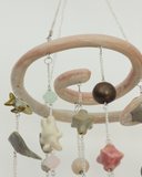 A hanging decorative mobile made from ceramic mini sculpts, small natural stones and bead charms on silver chains, photographed against a plain gray background.