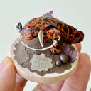 Sculpture of a orange and brown striped salamander standing on a wooden base and holding a kusarigama.