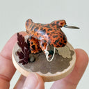 Sculpture of a orange and brown striped salamander standing on a wooden base and holding a kusarigama.