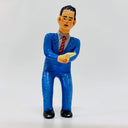 Clay sculpture of a business man wearing a blue suit with a gray shirt, red tie and holding a yellow notice in both hands, with a slightly worried expression.