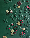 A dark green textured panel decorated with scattered clover shapes in dark green, cream, beige, and dark brown, interspersed with small red ladybugs.